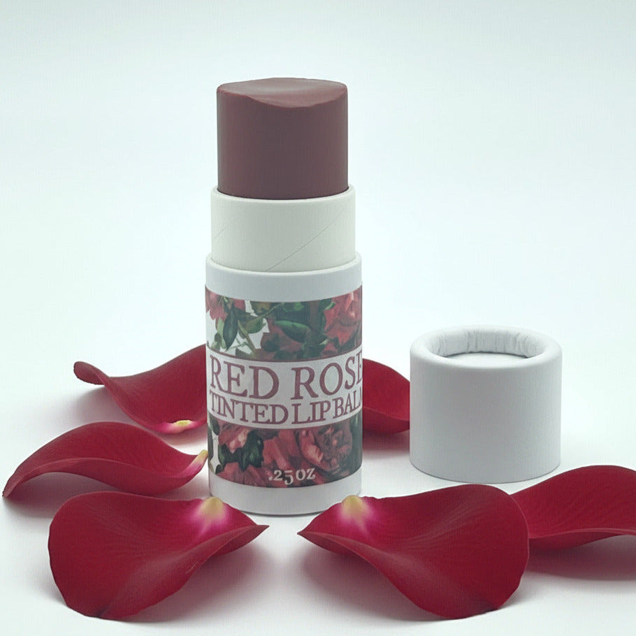 A 25ml stick lip balm with its cap removed, showing the dark reddish-brown tinted balm inside. The label reads 'RED ROSE TINTED LIP BALM' with a rose pattern, set against a plain white background.