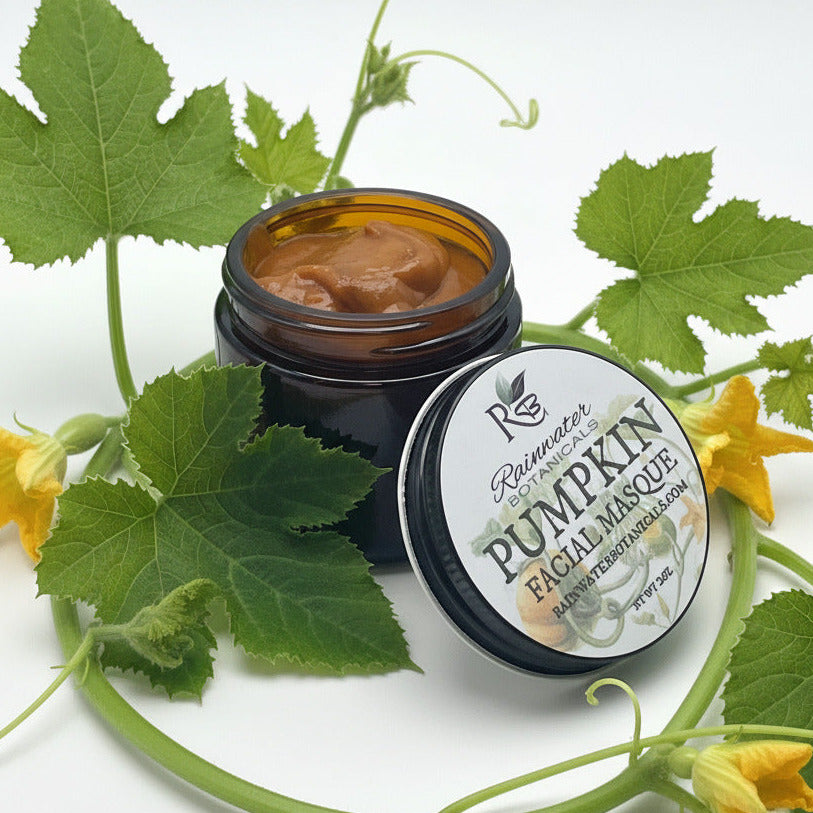 An open dark amber jar of Rainwater Botanicals Pumpkin Facial Masque, showing the thick orange-brown product inside, with its matching lid placed in front on a clean white background.